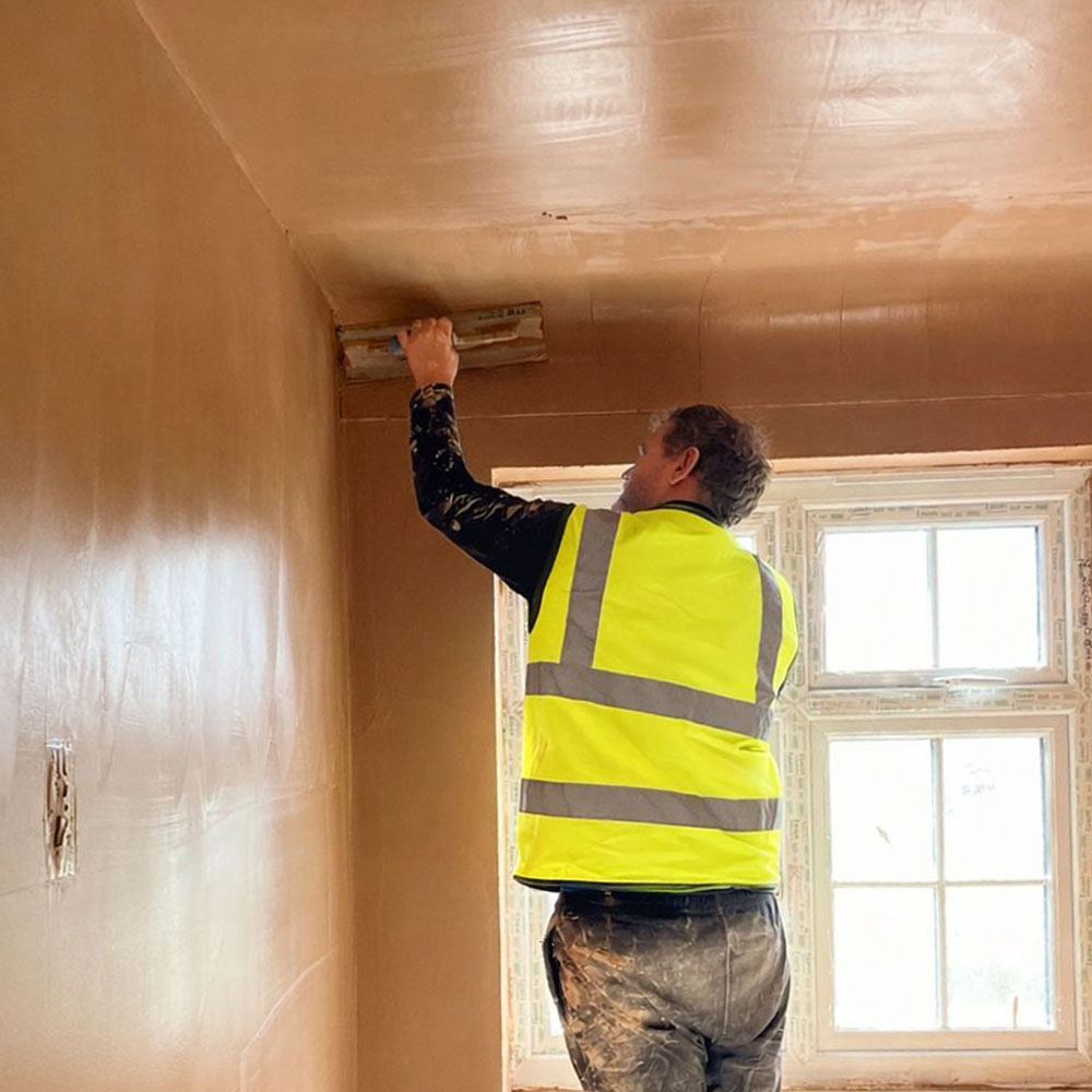 Mican Plastering team member applying plaster to the top of a property wall.
