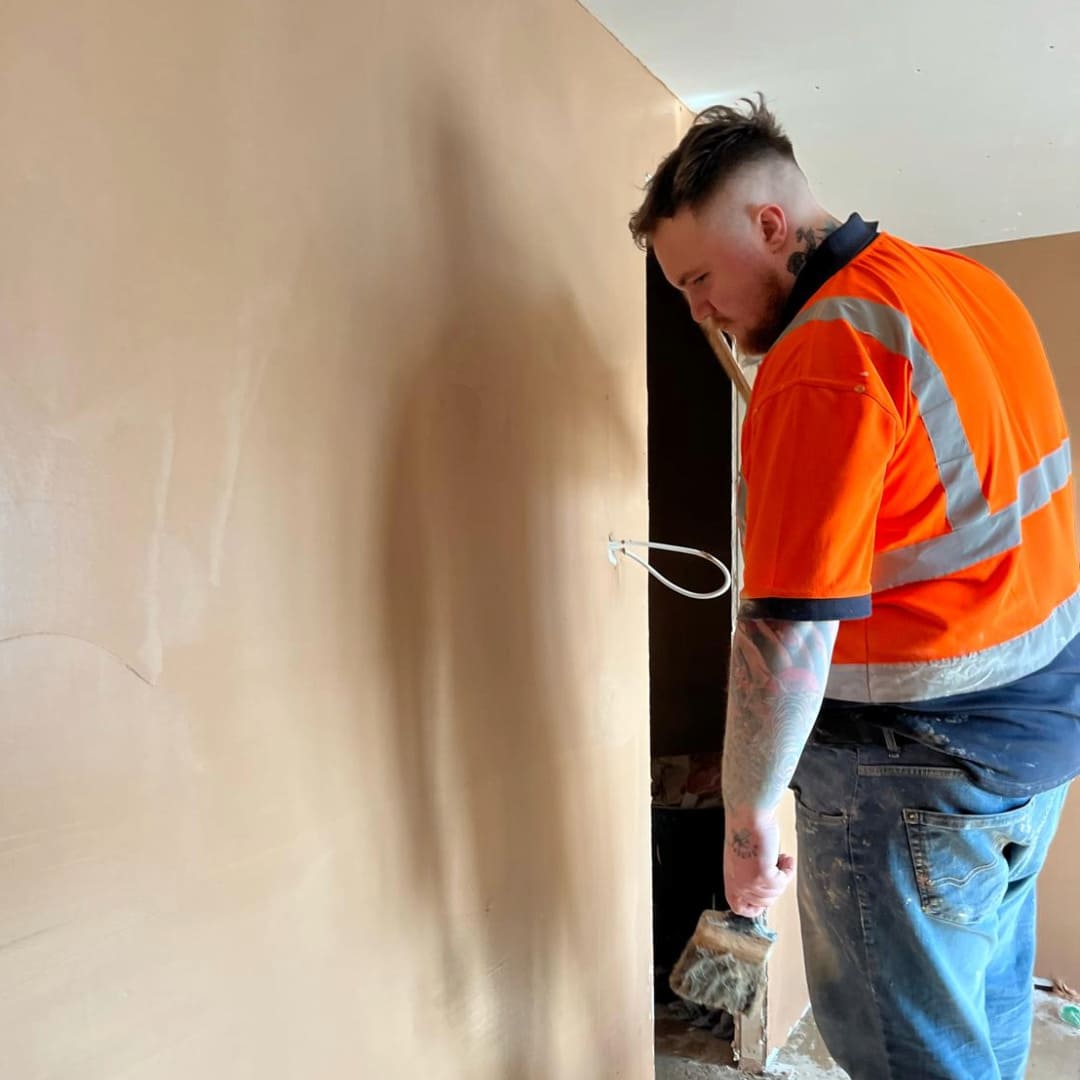 Mican Plastering contractor with high-visibility workwear skim finish dry lining a wall inside a home in Cheshire
