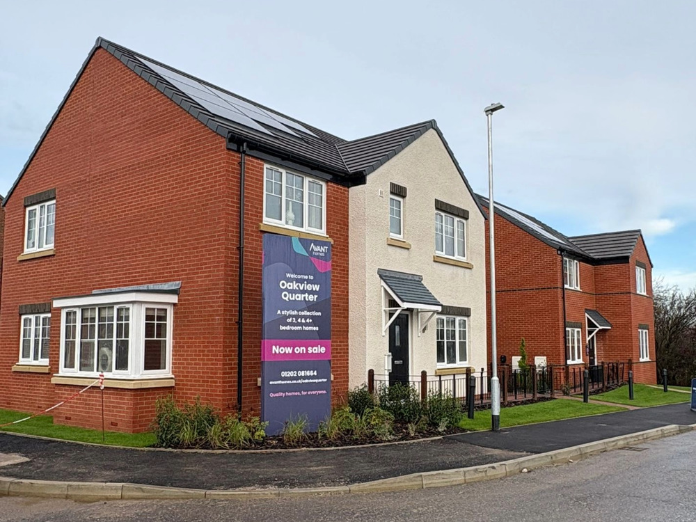 Side view of two new build brick houses with external rendering at Oakview Gardens, including a sign next to the road promoting the development